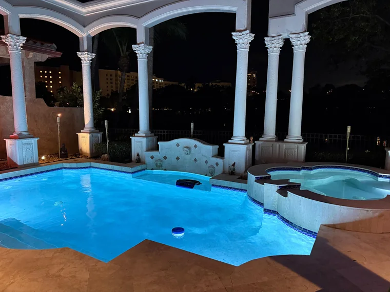 Pool and spa lit at night under a columned loggia